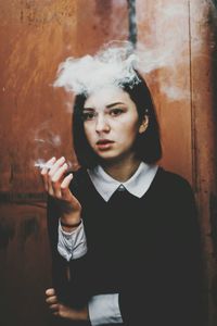Young woman smoking against rusty wall