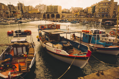 Boats moored in harbor by city against sky