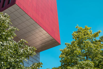 Red angular building against blue sky and trees 