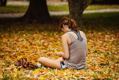 Rear view of woman sitting on fallen dry leaves at park during autumn