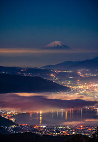 Illuminated city by sea against sky at sunset