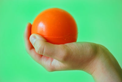 Close-up of hand holding red tomato over green background