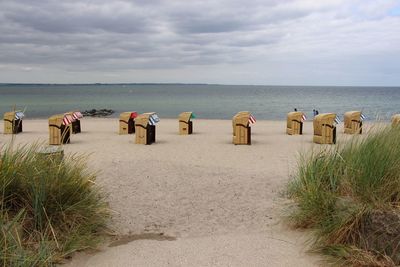 Hooded chairs on beach against sky