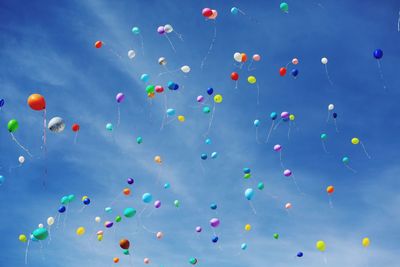 Low angle view of colorful helium balloons moving up in blue sky