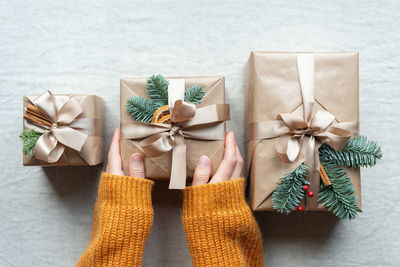 Women's hands hold a beautifully wrapped christmas present, decorated with natural decor and ribbon.