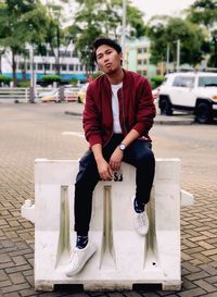 Portrait of young man sitting on barricade in city