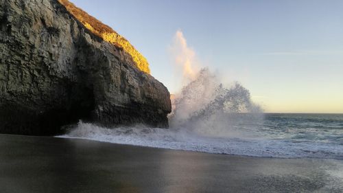 Wave splashing on rock formation at beach against sky