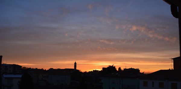 Silhouette of houses against cloudy sky during sunset