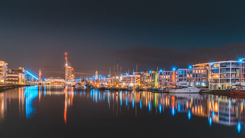 Illuminated buildings by river against sky at night