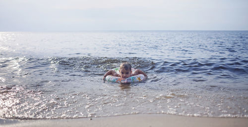 Little boy with flotation ring swimming at sea in sunset light, lots of splashes and happiness