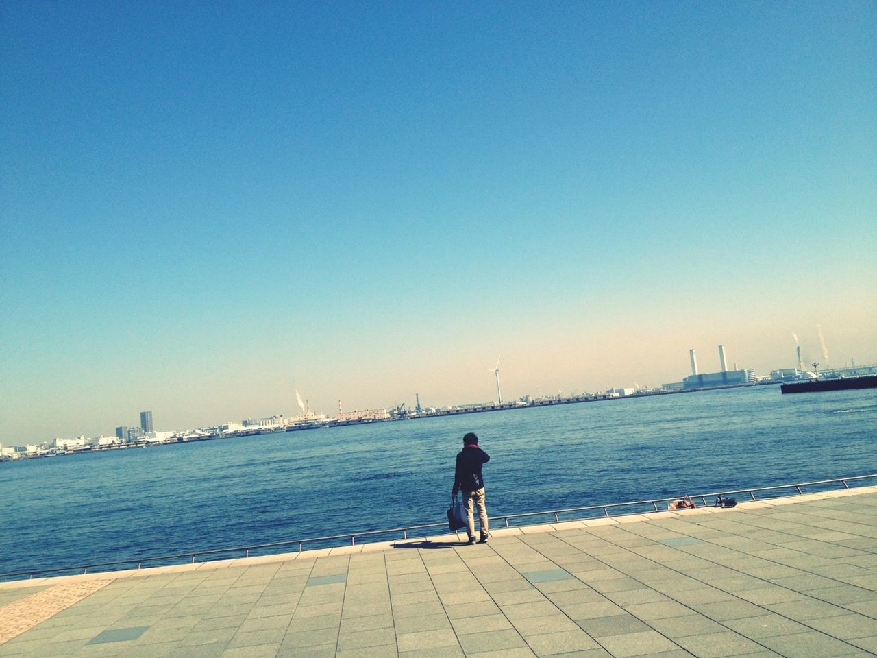 clear sky, water, copy space, sea, rear view, blue, full length, men, lifestyles, leisure activity, standing, pier, built structure, person, architecture, sitting, outdoors, city