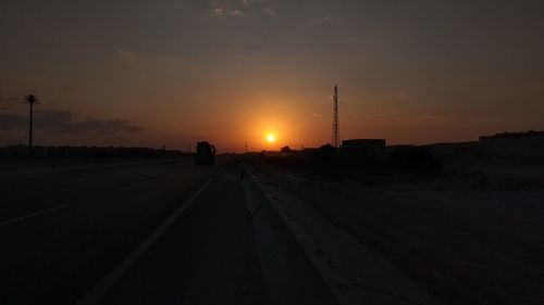 Road by silhouette city against sky during sunset