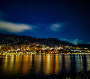 Illuminated city by mountains against sky at night