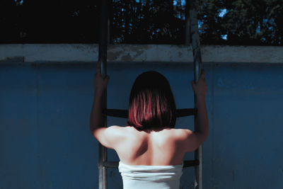 Rear view of woman climbing on ladder against wall