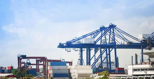 Cranes at harbor against sky
