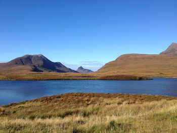 Scenic view of lake and mountains against clear blue sky