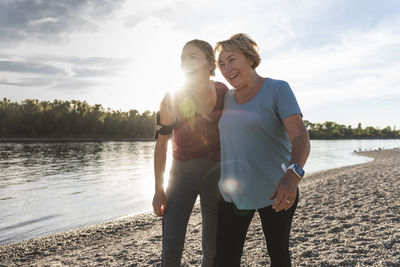 Fit grandmother and granddaughter walking at the river with arms around, having fun