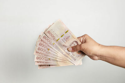 Cropped hand holding paper currency against white background