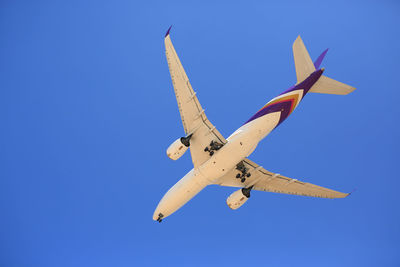 Low angle view of airplane flying against clear blue sky