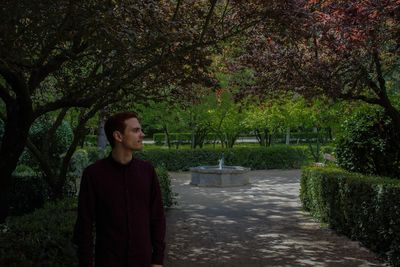 Young woman standing on footpath by trees at park