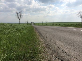 Road passing through field against cloudy sky