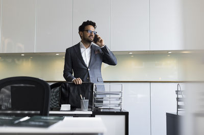 Male real estate agent talking on smart phone at desk in office