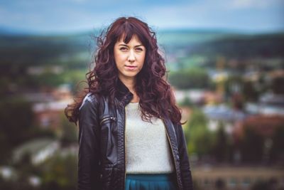 Portrait of smiling woman with curly hair standing against townscape