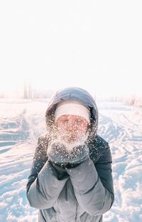 Girl blows snow from mittens in sunny cold weather