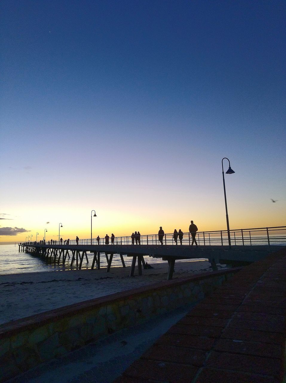 SILHOUETTE PEOPLE ON FOOTPATH BY SEA AGAINST CLEAR SKY