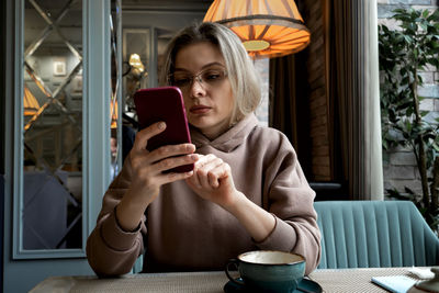 Caucasian middle-aged blonde woman sits in a cafe, drinks coffee and talks on a mobile phone