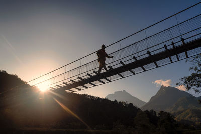 Silhouette man walking on bridge against sky during sunset
