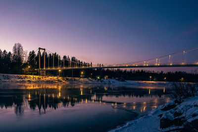 Illuminated bridge over river against sky at night