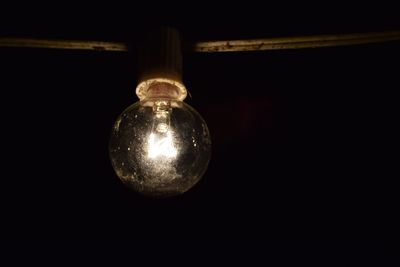 Close-up of light bulb hanging against black background