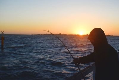 Silhouette man fishing in sea against sky during sunset