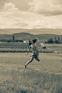 Full length of woman jumping on field against mountain