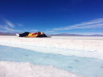 Young woman lying on salt flat against blue sky