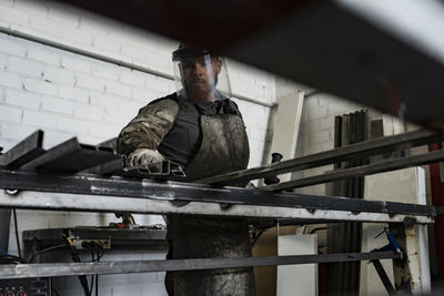 Serious male worker in dirty apron standing at workbench and preparing metal details for welding