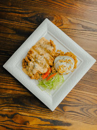 Fried noodles with fried egg on a white plate served with cheese sauce