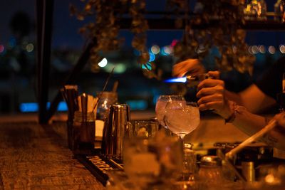 Cropped hands of bartender with drinks on holding lighter in restaurant at night 
