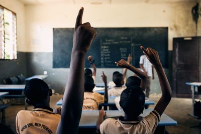 Rear view of students with arms raised sitting in classroom