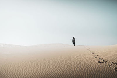 Person walking on desert against clear sky