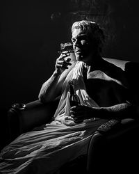 Woman looking away while sitting against black background