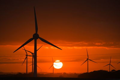 Silhouette wind turbines on field against sky during sunset