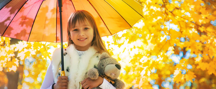 Portrait of cute girl holding umbrella against maple tree