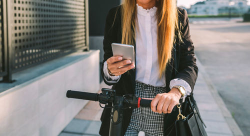 Midsection of woman using mobile phone in city