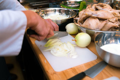 The cook slices onions with a large knife. the ingredients are in bowls on the table.