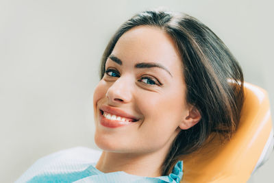 Close-up portrait of smiling patient sitting on chair in dentist office