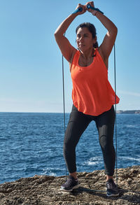Fitness woman in sports set training with elastic band,weights gym exercises, in front of the water	