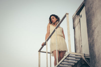 Low angle view of thoughtful young woman looking away while standing on building terrace during sunset