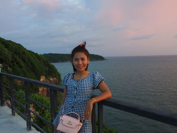 Portrait of smiling girl standing by railing against sea